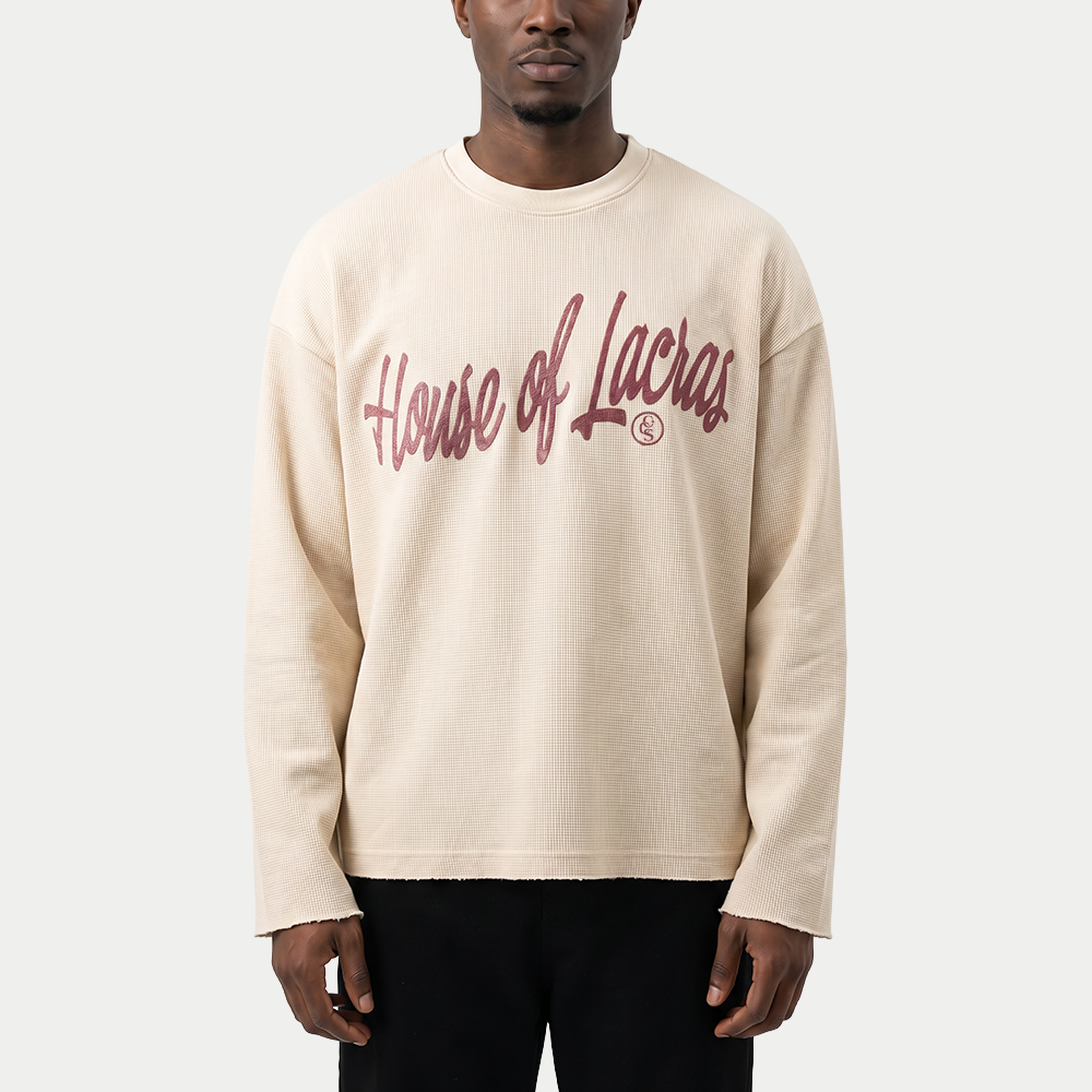 Man wearing the cream House of Lacras waffle knit long sleeve tee by Caracas Merch with black trousers